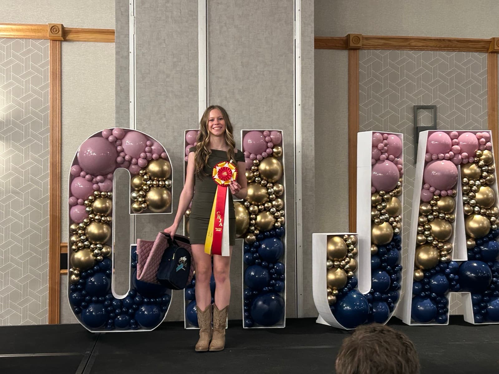 Tully holding a ribbon in front of oversized CHJA letters at the Colorado Hunter Jumper Association year-end awards.