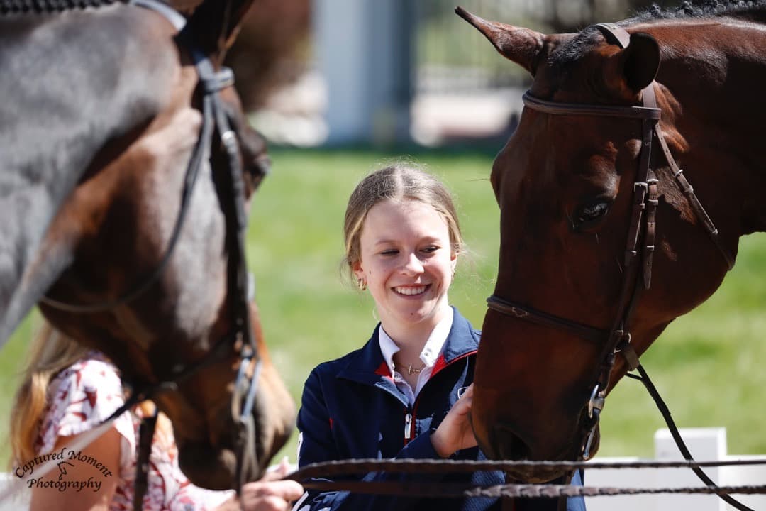 Tully smiling between two horses nose-to-nose at a show.