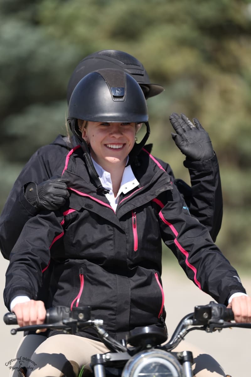 Tully waving while riding a scooter around the show grounds in her riding gear.